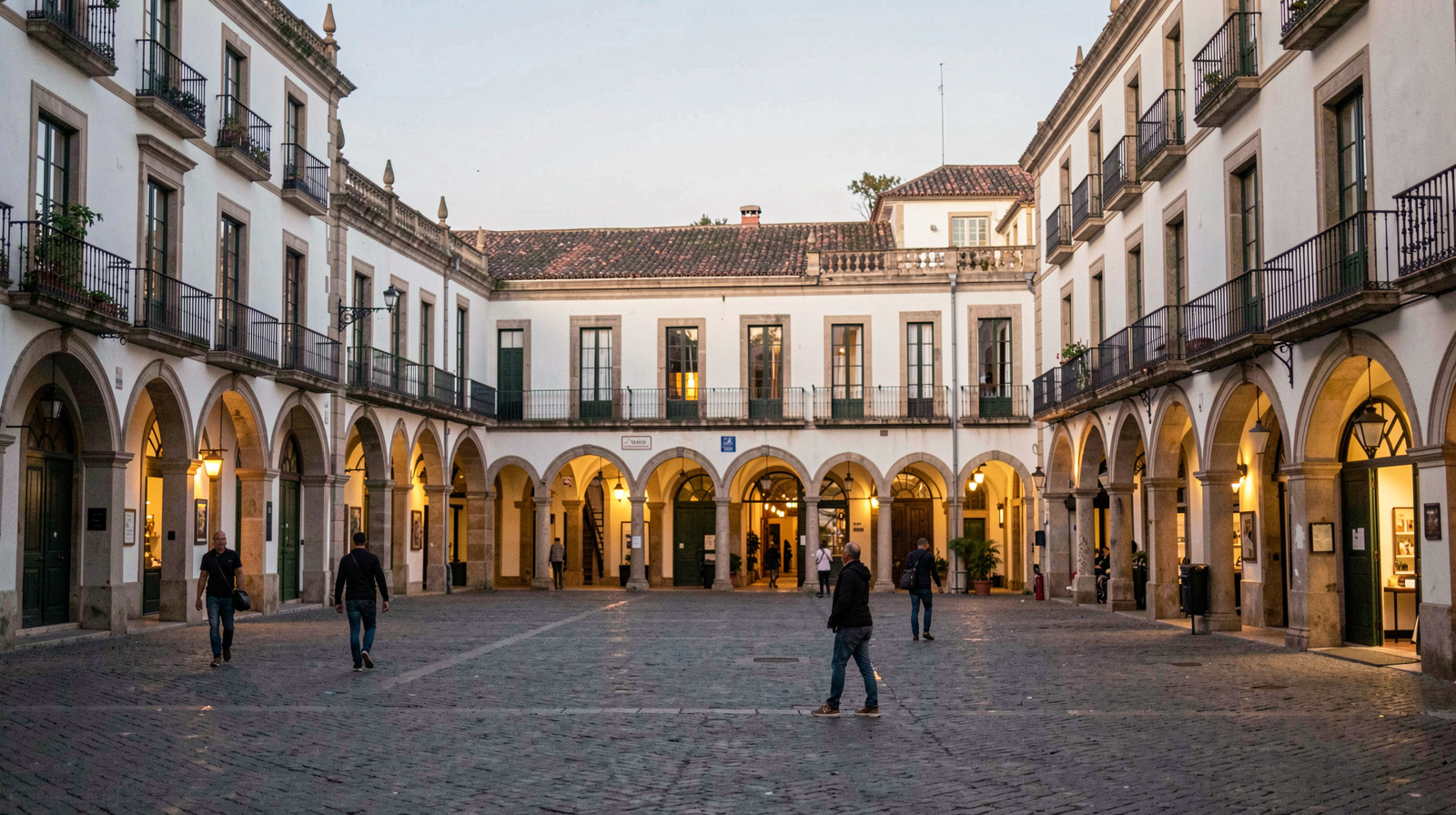 Vue de la plaza Mayor de Valladolid au crépuscule, arcades éclairées, quelques passants, cadrage large depuis une rue latérale